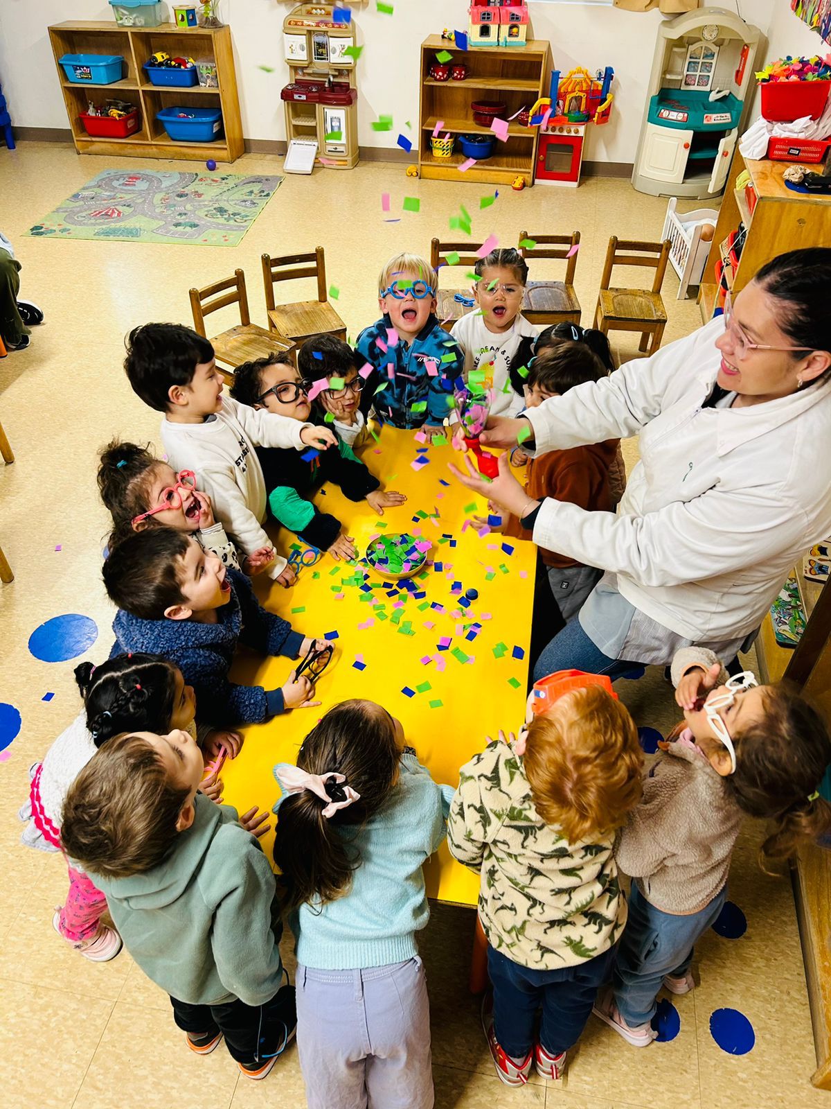 Niños haciendo collage con confeti en mesa amarilla
