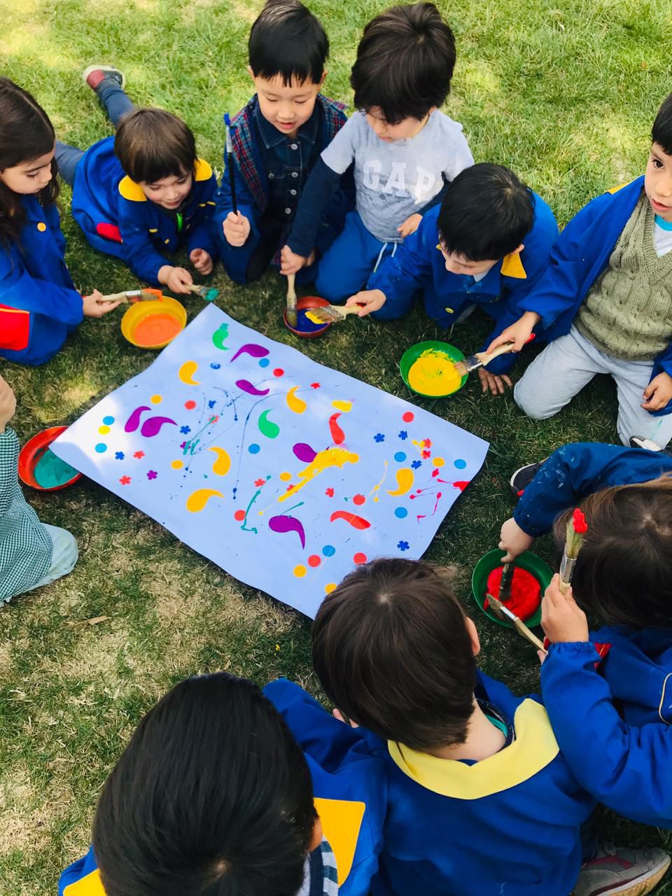 Niños pintando lienzo grupal en el pasto