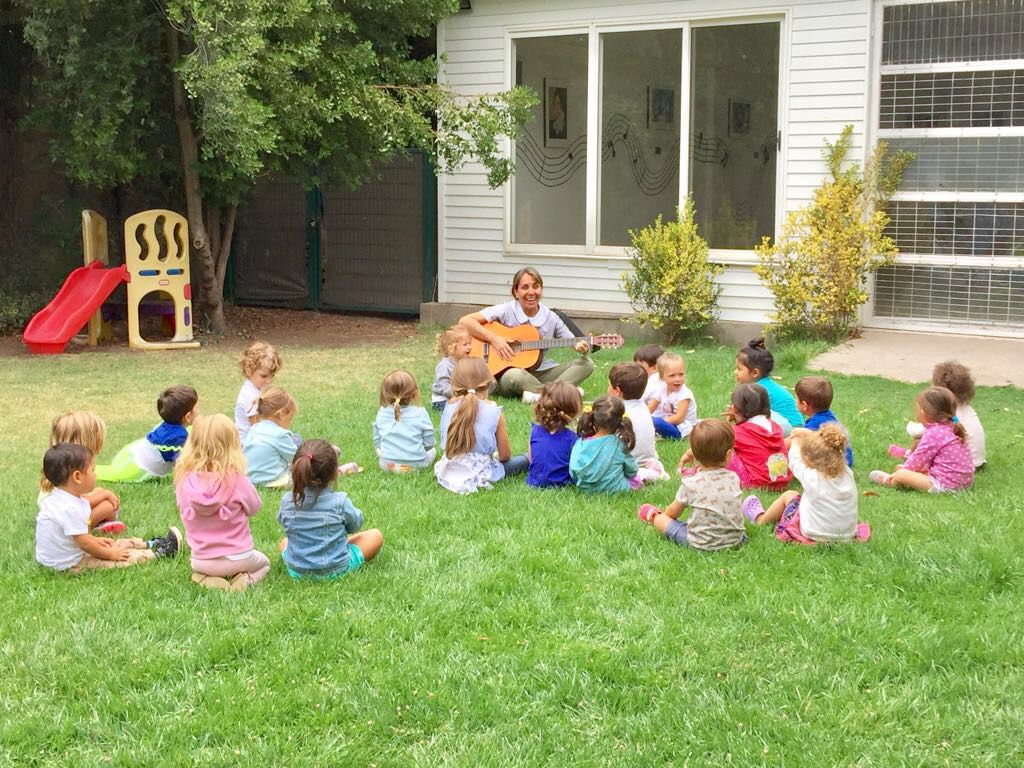 Tía tocando guitarra para grupo de niños en el pasto
