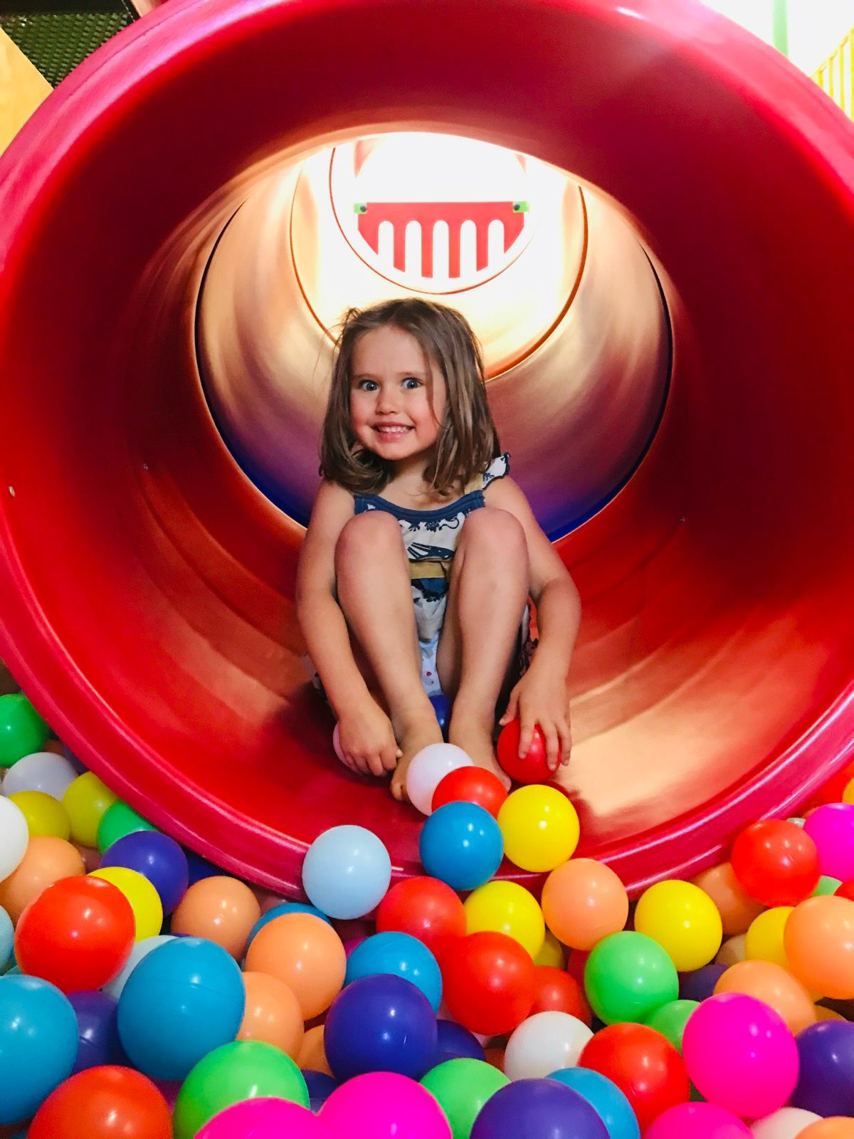 Niña en tubo del tobogán sobre piscina de pelotas